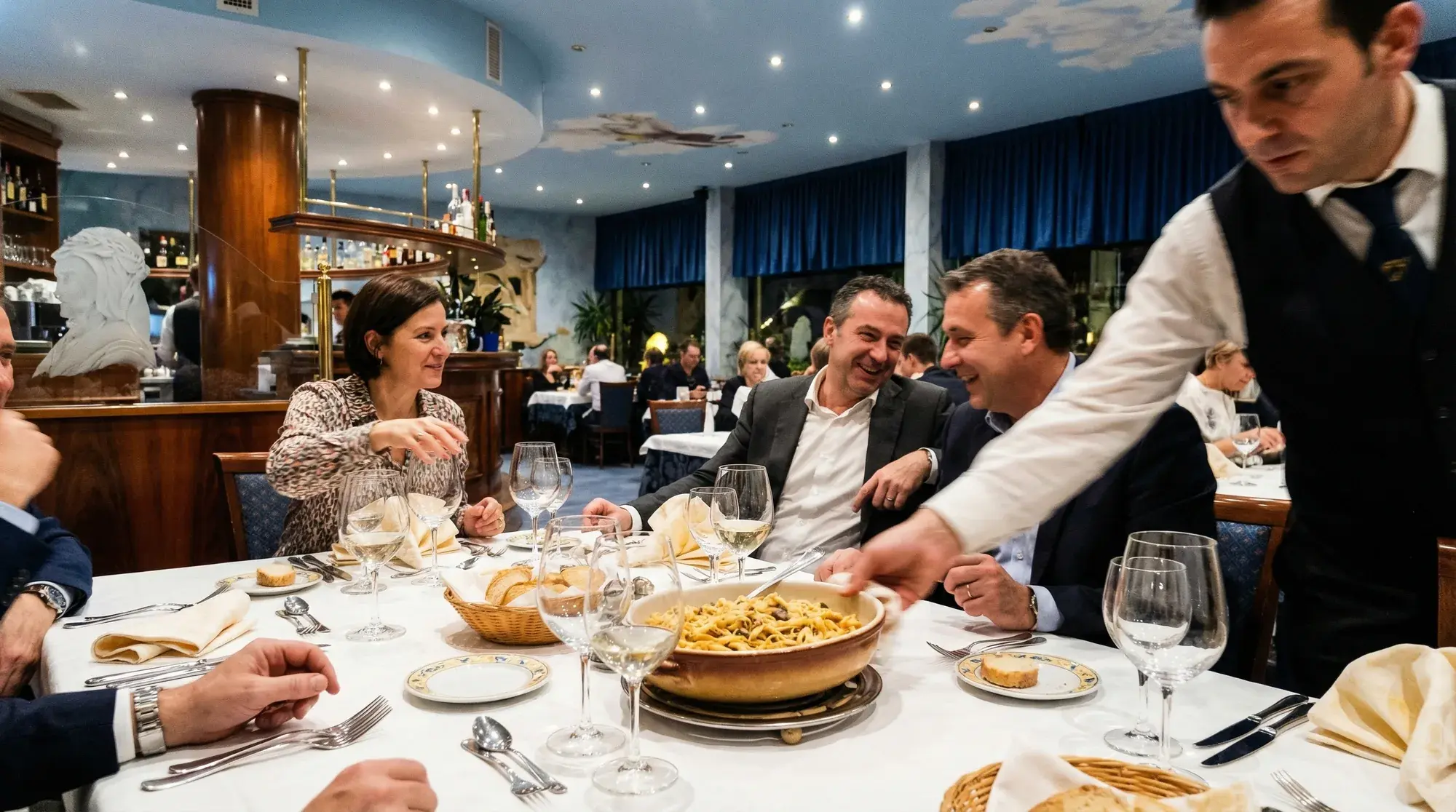 Service bringt Pasta an einen festlich gedeckten Tisch bei La Commedia.
