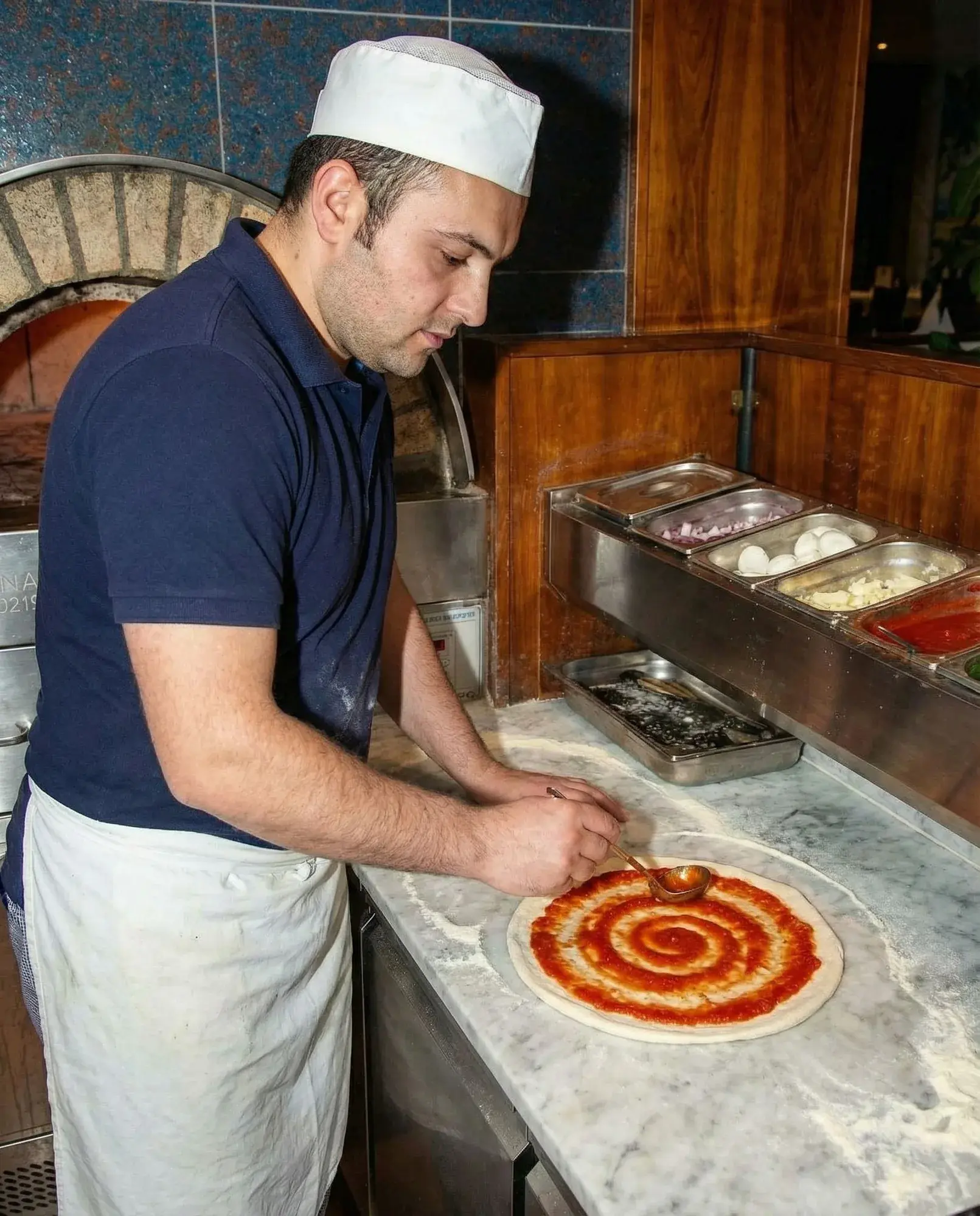 Tomatensauce wird auf dem Pizzateig verteilt.